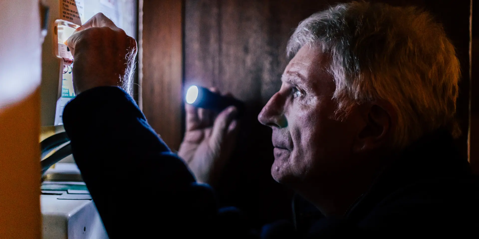 Older man with a torch inspecting a fuse box after a power cut