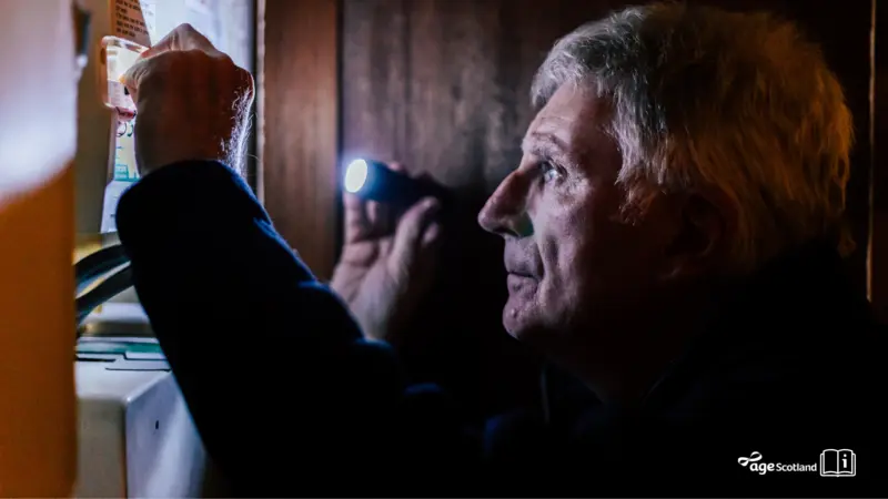 Older man with a torch inspecting a fuse box after a power cut